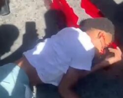 Two fast-riding young men on motorcycle fall under banana truck